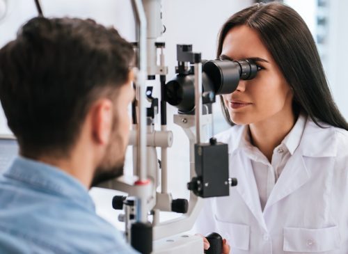Female optometrist using an ophthalmic device to examine a male patient's eyes.