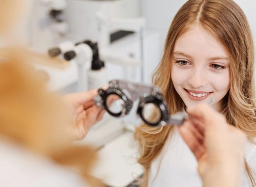 Young girl smiling while an optometrist holds a trial frame for an eye exam.