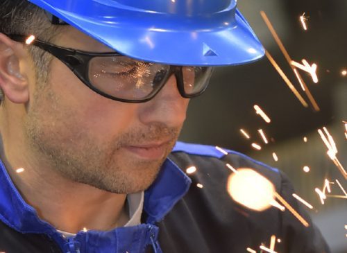 Man wearing safety glasses and a blue hard hat while working with metal sparks flying.
